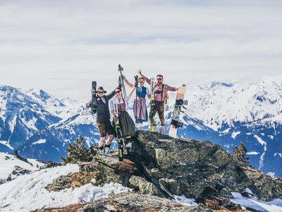 Winterfreuden in Gerlos • Der Grubacher: Winterurlaub Zillertal Vier Personen in Trachten mit Ski- und Snowboardausrüstung auf schneebedecktem Berg