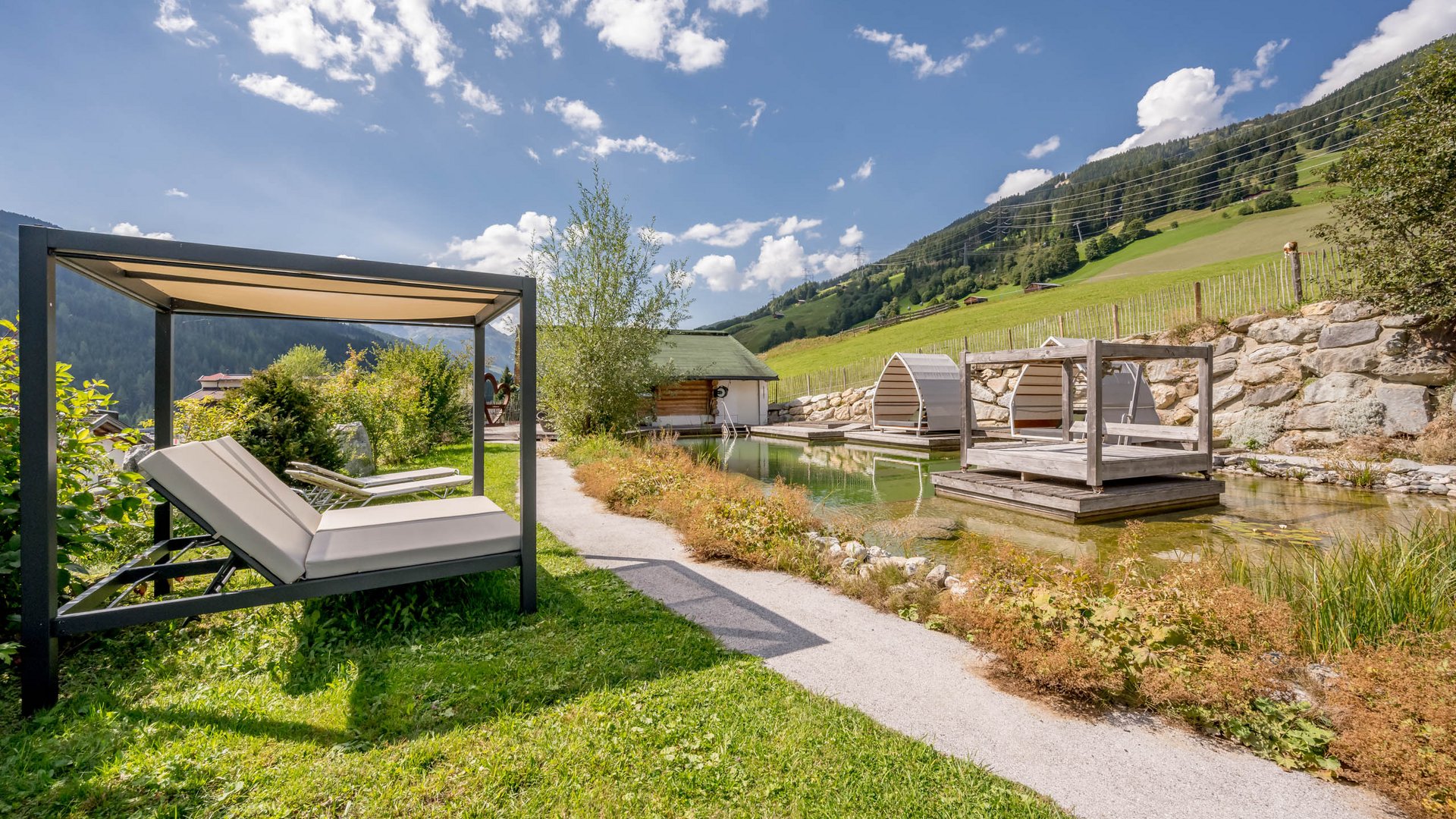 Private Wohlfühlmomente • Der Grubacher: Biohotel in Gerlos Garten mit Schwimmteich, Liegeflächen und Holzplattform im Sommer