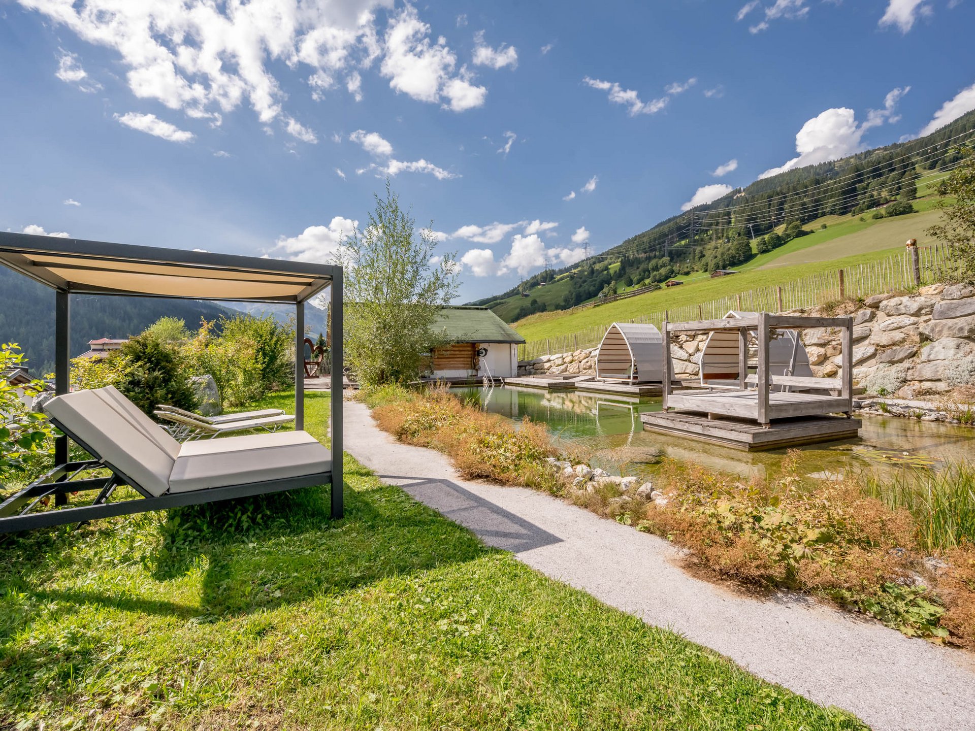 Der Grubacher • Biohotels in Gerlos im Zillertal in Tirol Garten mit Schwimmteich, Liegeflächen und Holzplattform im Sommer