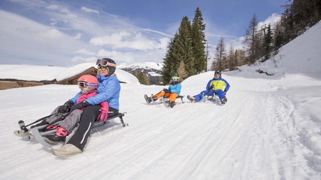 Pictures & Impressions • Der Grubacher: Hotel in Gerlos Family sledding laughing on a snowy slope with a winter landscape in the background