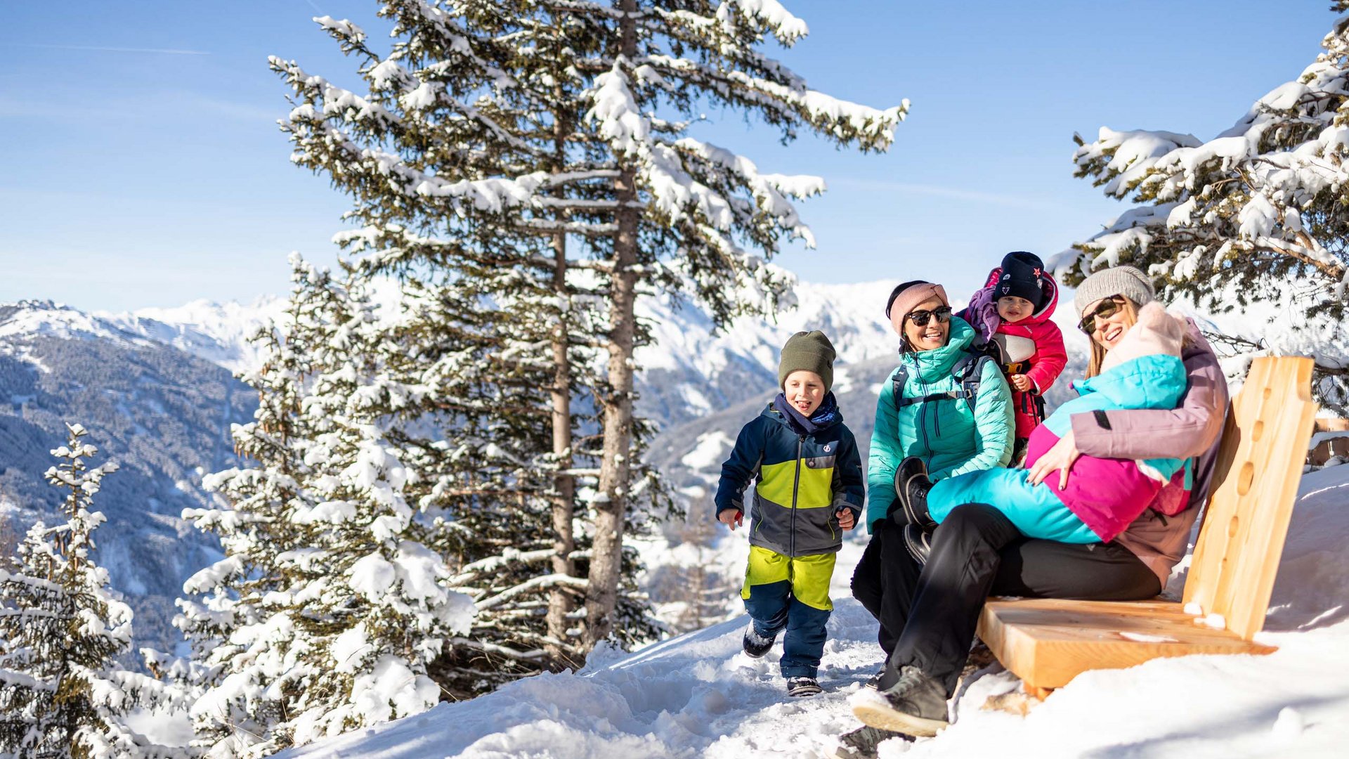 Erlebnisse im Zillertal • Der Grubacher: Biohotel in Gerlos Familie macht Pause auf Winterwanderung mit Blick auf verschneite Alpenlandschaft