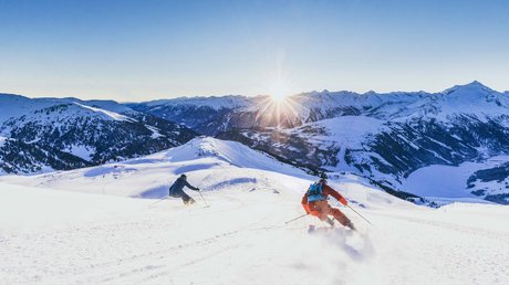 Pictures & Impressions • Der Grubacher: Hotel in Gerlos Two skiers carve through fresh powder snow at sunset