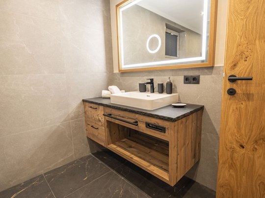 Grubi's Freizeitwohnsitz • Der Grubacher Modernes Badezimmer mit Holzbadmöbeln und beleuchtetem Wandspiegel