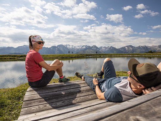 Erlebnisse im Zillertal • Der Grubacher: Biohotel in Gerlos Pärchen entspannt auf einer Holzliege am Bergsee