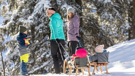 Pictures & Impressions • Der Grubacher: Hotel in Gerlos Two women pull children on sleds through a snowy winter forest