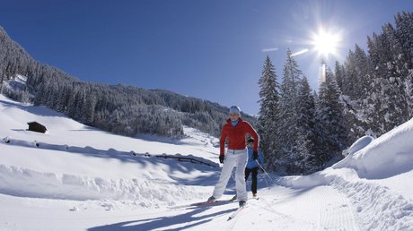 Pictures & Impressions • Der Grubacher: Hotel in Gerlos Cross-country skiers glide through a snowy winter landscape in sunshine at the edge of the forest