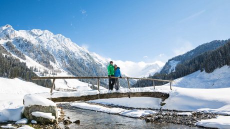 Pictures & Impressions • Der Grubacher: Hotel in Gerlos Couple on a snowy wooden bridge with a view of the majestic alpine landscape in winter