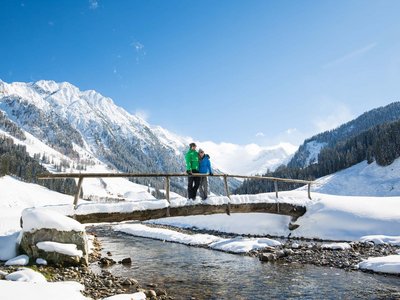Erlebnisse im Zillertal • Der Grubacher: Biohotel in Gerlos Paar auf verschneiter Holzbrücke mit Blick auf majestätische Alpenlandschaft im Winter