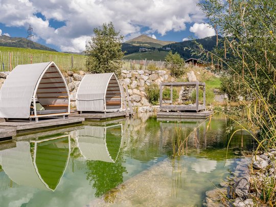Wasserwelt in Gerlos • Der Grubacher: Biohotel in Tirol Schwimmteich im Garten mit Gartenliege und Blick auf die Berge