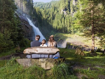 Rund um Gerlos • Der Grubacher: Biohotel in Tirol Familie auf einer Bank im Wald mit Blick auf den Wasserfall