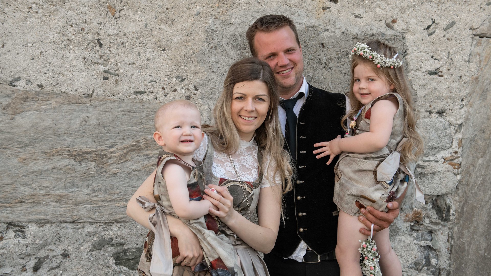 Gasgeberfamilie in Tracht vor Steinmauer