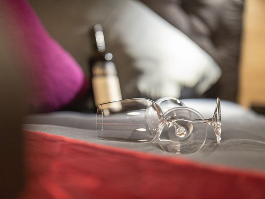 Grubi's Freizeitwohnsitz • Der Grubacher Zwei leere Weingläser und eine Weinflasche auf Bett mit grauer Decke und roten Akzenten