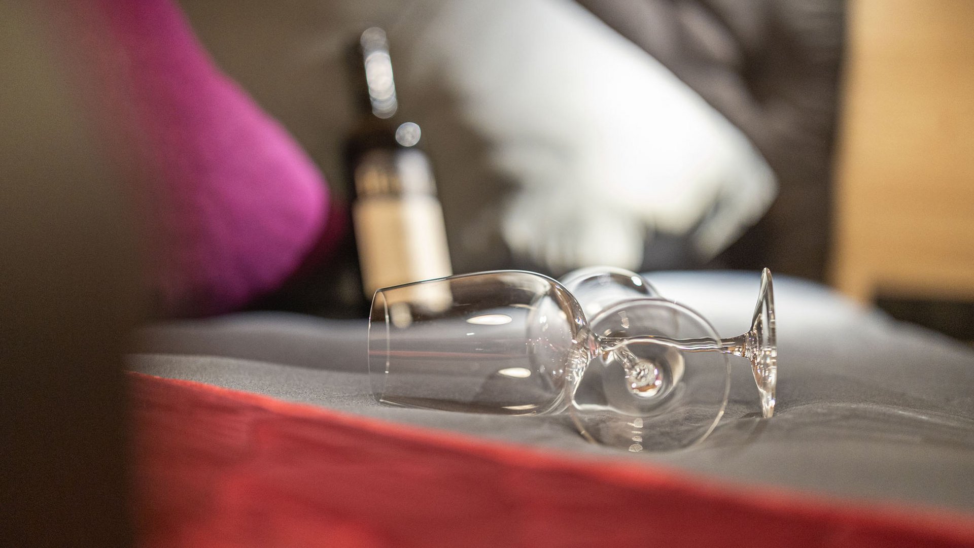 Grubi's Freizeitwohnsitz • Der Grubacher Zwei leere Weingläser und eine Weinflasche auf Bett mit grauer Decke und roten Akzenten