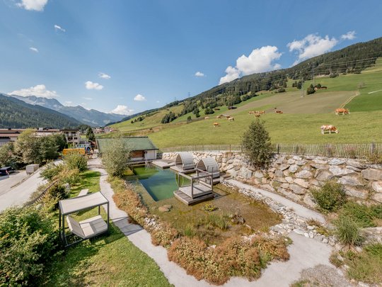 Wasserwelt in Gerlos • Der Grubacher: Biohotel in Tirol Garten mit Schwimmteich, Liegeflächen und Blick auf die Kuhweide