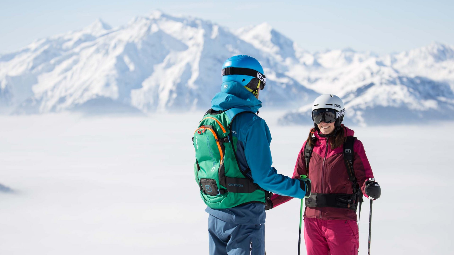Zwei Skifahrer unterhalten sich vor einer beeindruckenden Winterkulisse über den Wolken