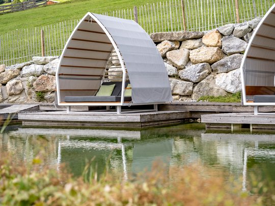 Wasserwelt in Gerlos • Der Grubacher: Biohotel in Tirol Gartenliegen am Schwimmteich mit Blick auf die Wiese
