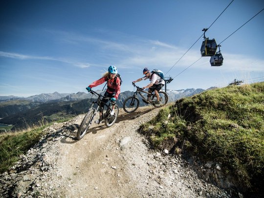 Erlebnisse im Zillertal • Der Grubacher: Biohotel in Gerlos Pärchen auf einem Radweg in den Bergen mit Seilbahn